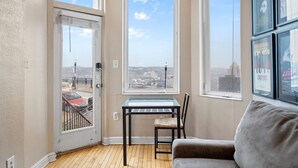 Una habitación con una mesa de vidrio, una silla y un sofá. Hay dos ventanas con vistas a la ciudad.
