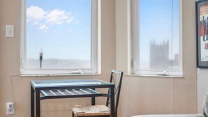 Una habitación con una mesa y una silla cerca de una ventana, una lámpara y un cuadro en la pared.