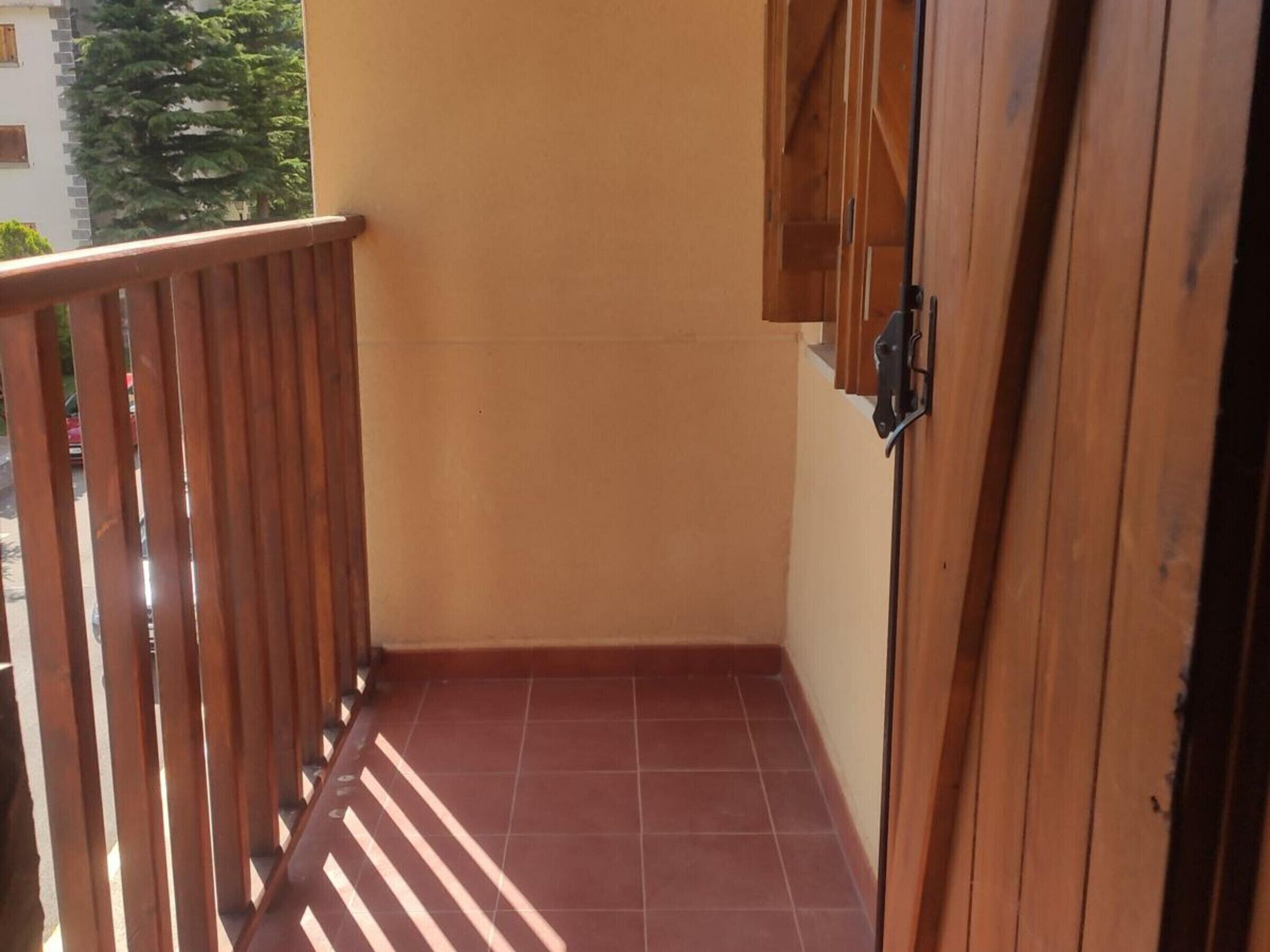 A narrow balcony with a wooden railing, a tiled floor, and a door with a black handle.