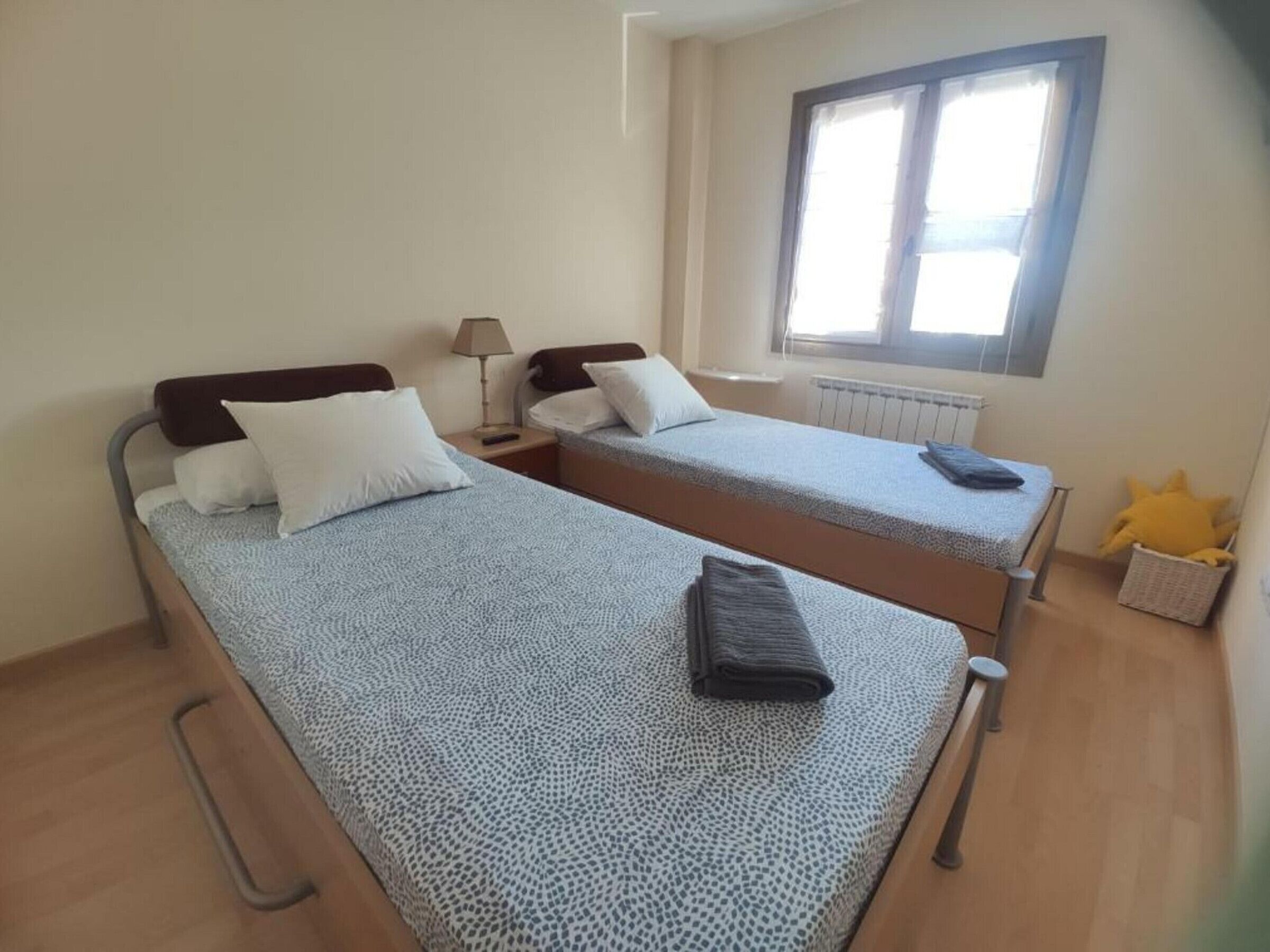 Une chambre avec deux lits simples, une fenêtre, un radiateur et une petite table avec une lampe.
