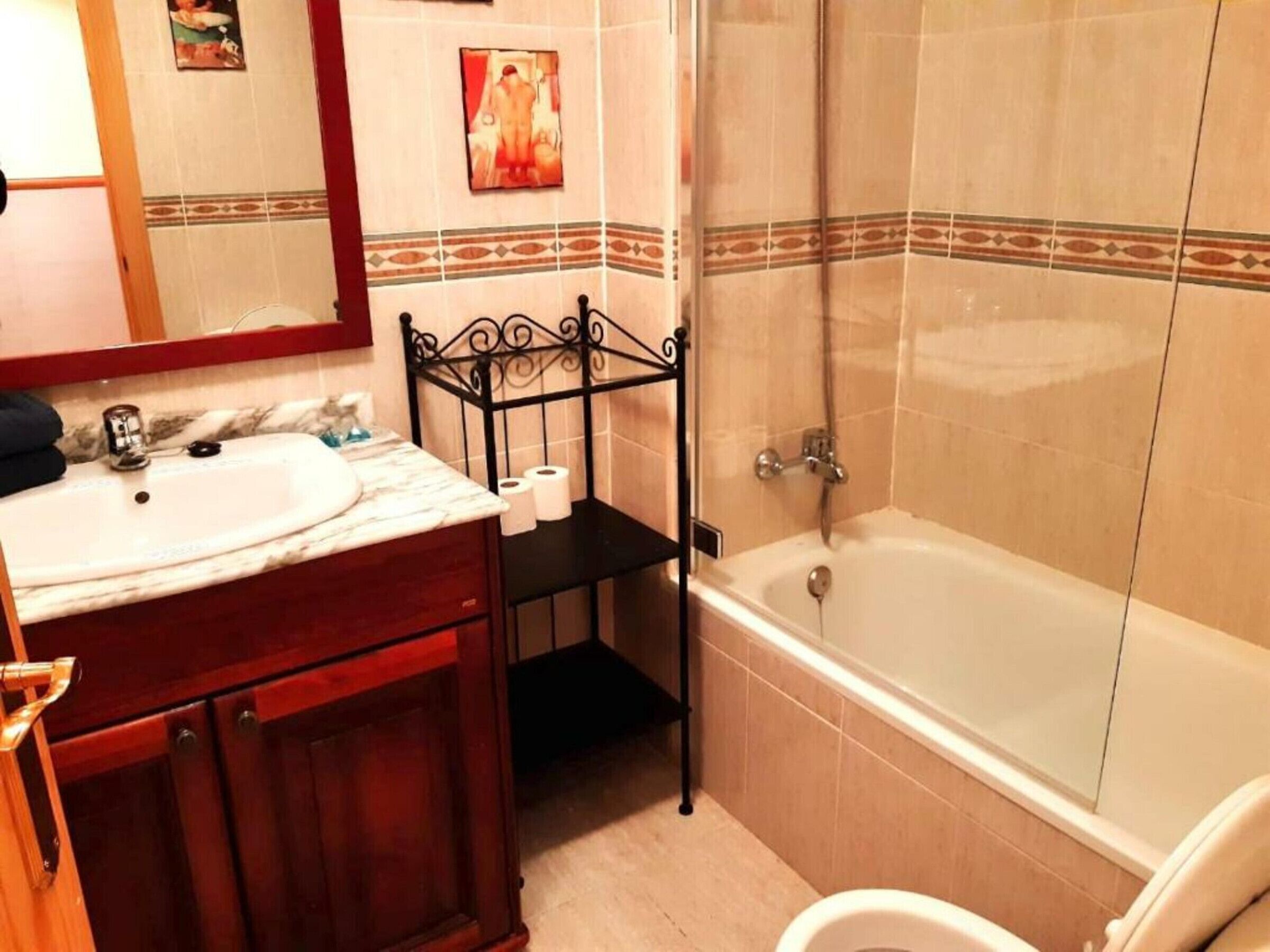 A bathroom with a marble sink, a black metal shelf, a toilet, and a bathtub.