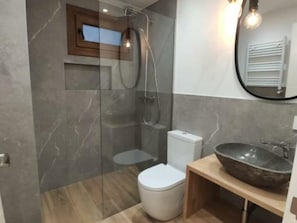 Bathroom features a glass-enclosed shower, handheld showerhead, and a wall-mounted faucet.