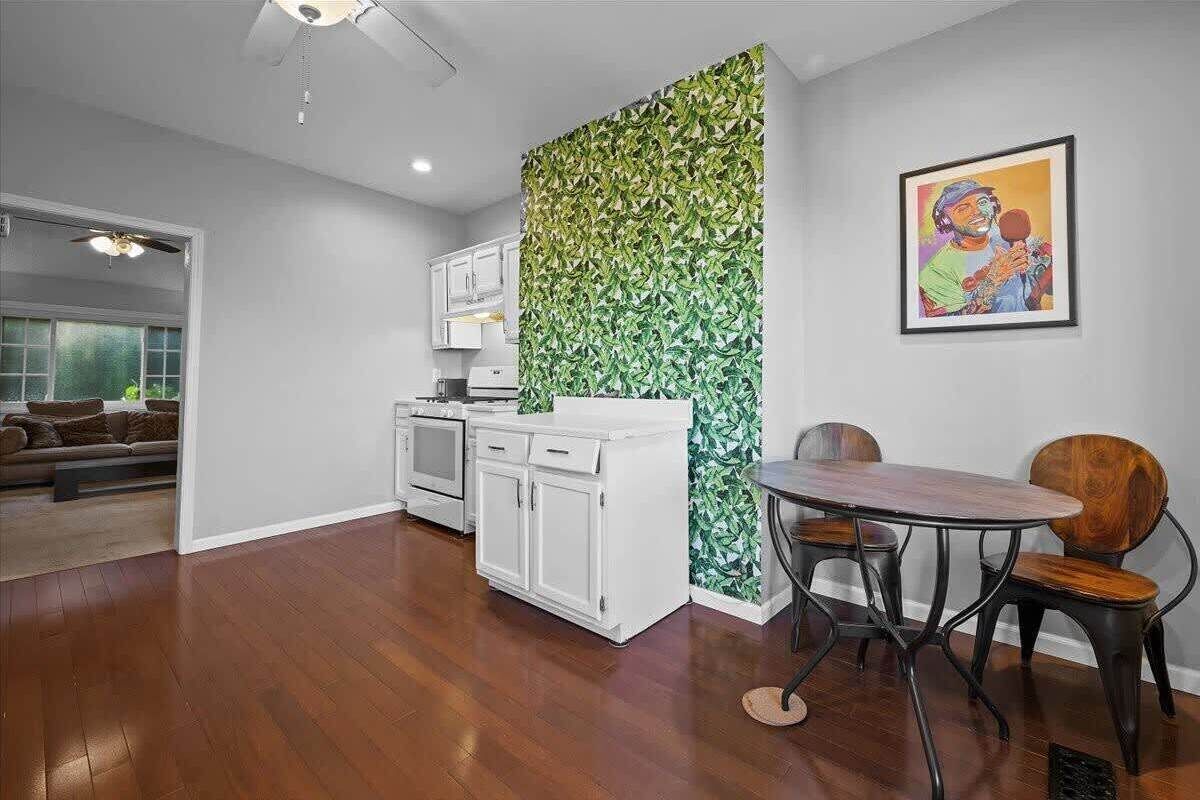 Une cuisine moderne avec des meubles blancs, un mur d’accent orné d’un motif de feuilles vertes, et un coin repas avec une table ronde et des chaises.