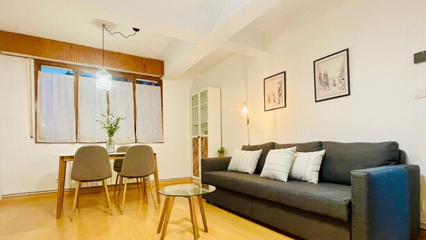 A modern living room with a sofa, two chairs, a glass coffee table, and a dining table. - Cozy 2BR Apartment with Pool in Jaca – Sleeps 6, 2 Bathrooms (Jaca)