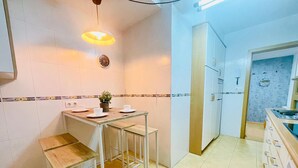A compact kitchen with a wooden table and stools, a hanging light fixture, and a clock on the wall. - Cozy 2BR Apartment with Pool in Jaca – Sleeps 6, 2 Bathrooms (Jaca)