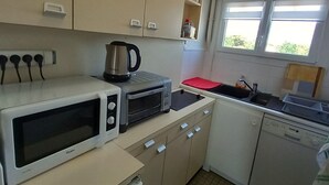 Ett kompakt kök med mikrovågsugn, brödrost, vattenkokare och diskmaskin. Köket har skåp med handtag och ett fönster som släpper in naturligt ljus.