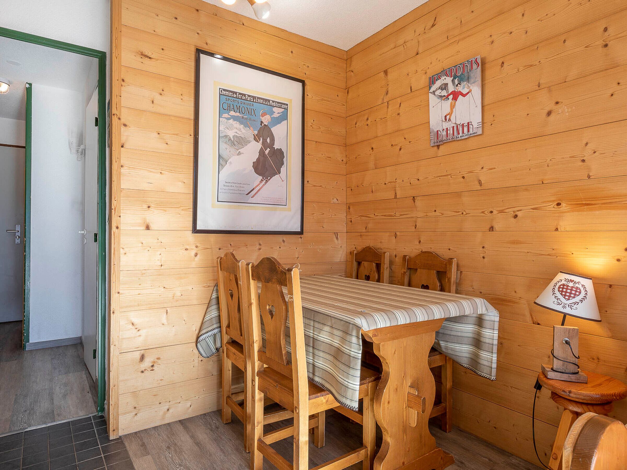 A wooden interior with a table and chairs, a framed poster, and a lamp.