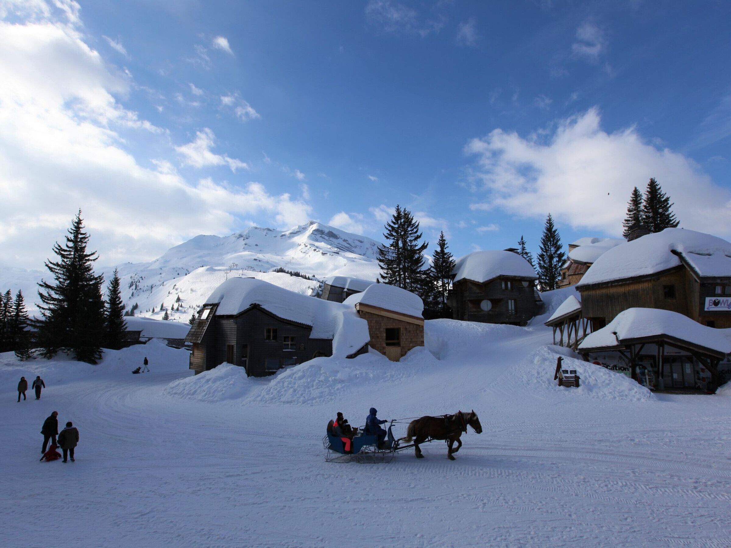 A snowy village with wooden buildings, a horse-drawn sleigh, and people walking.