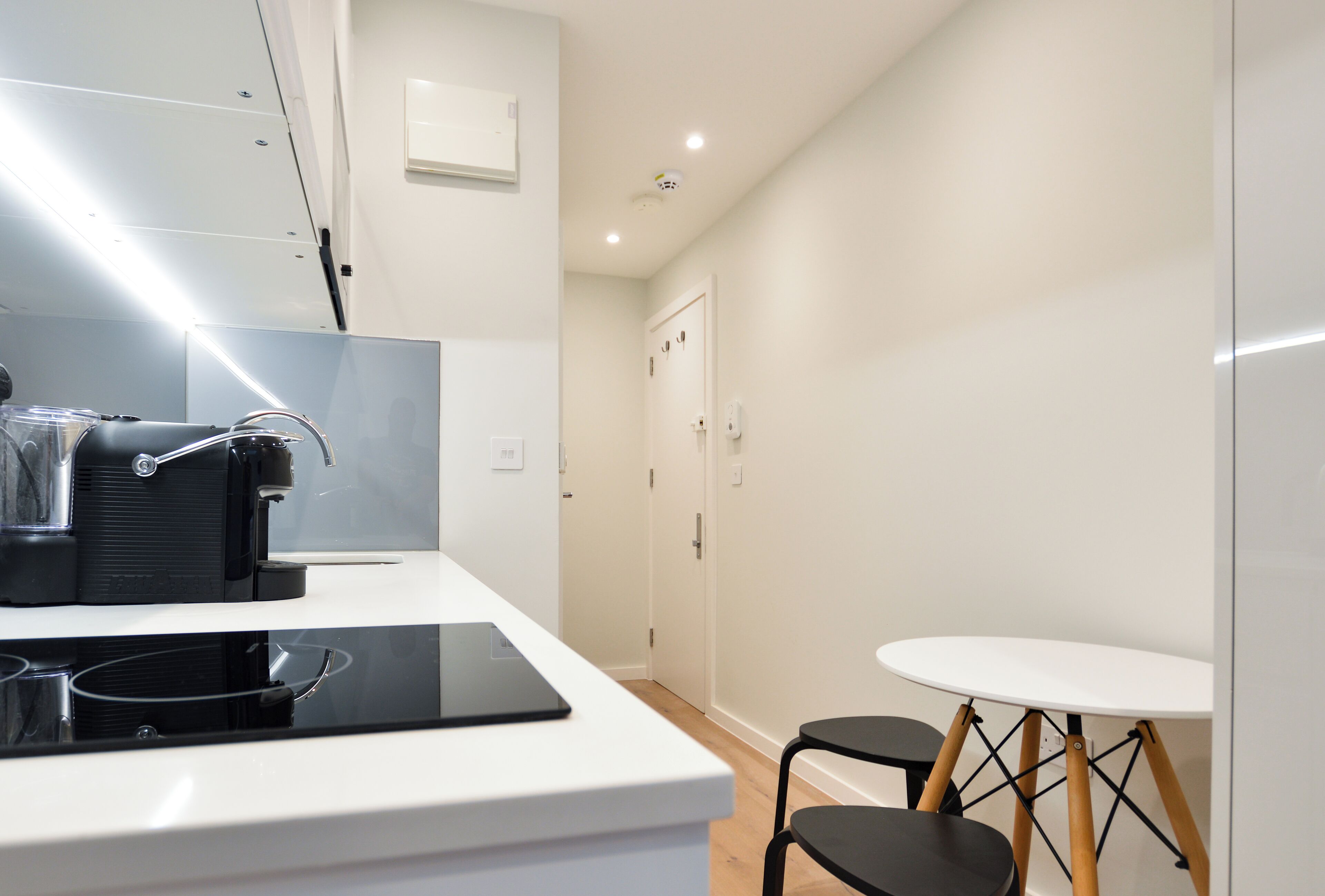 A modern kitchen with a white countertop, a black coffee machine, and a small round table with two chairs.