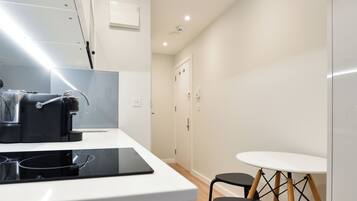 A modern kitchen with a white countertop, a black coffee machine, and a small round table with two chairs.