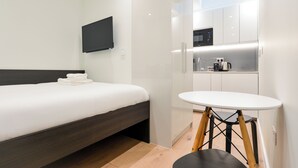 A modern hotel room with a bed, a flat-screen TV, a kitchenette, and a small round table. - StayPrime Fitzrovia Serviced Apartments (London)