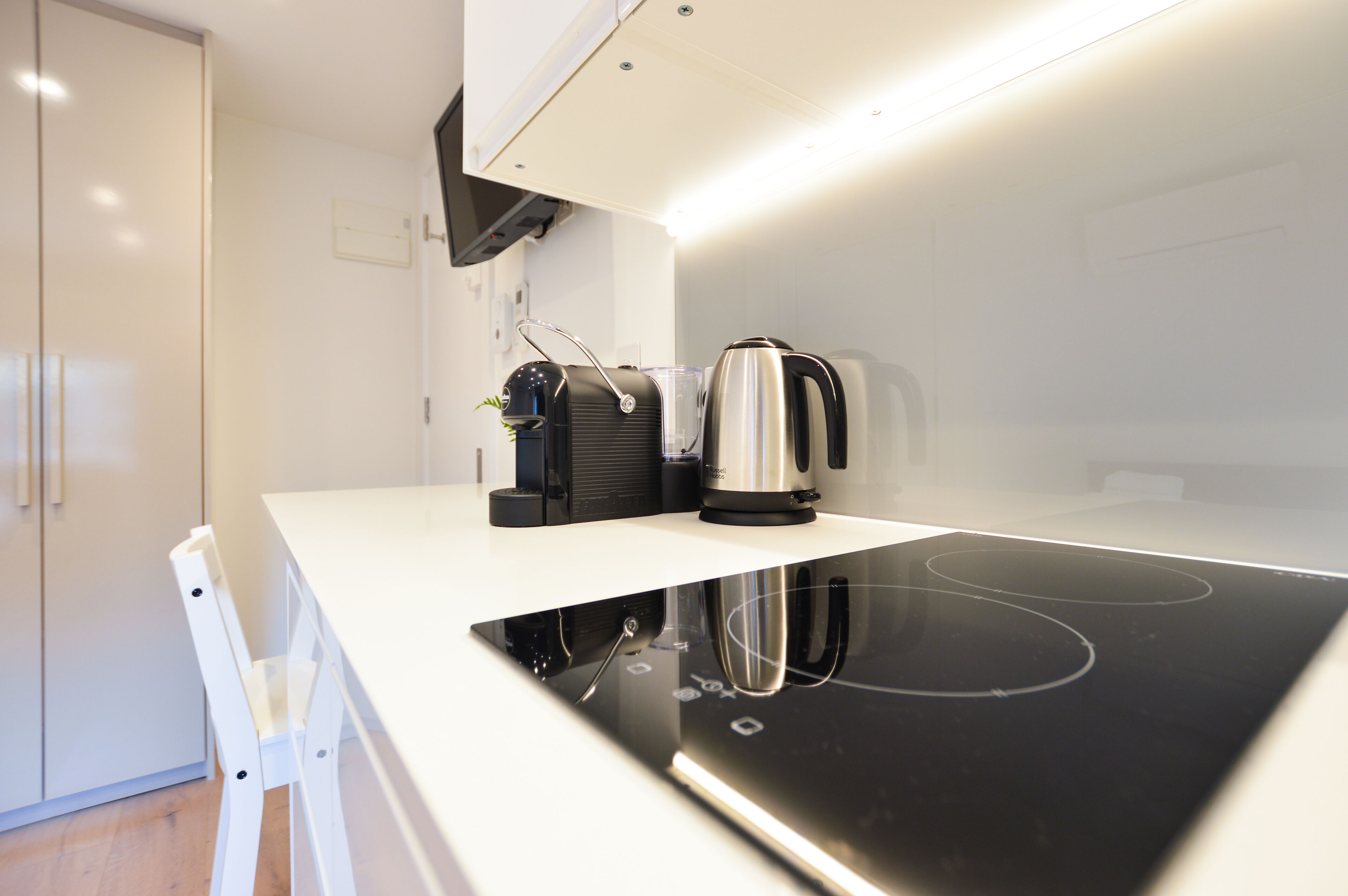 A modern kitchen with a white countertop, a black induction cooktop, a coffee maker, and a kettle.