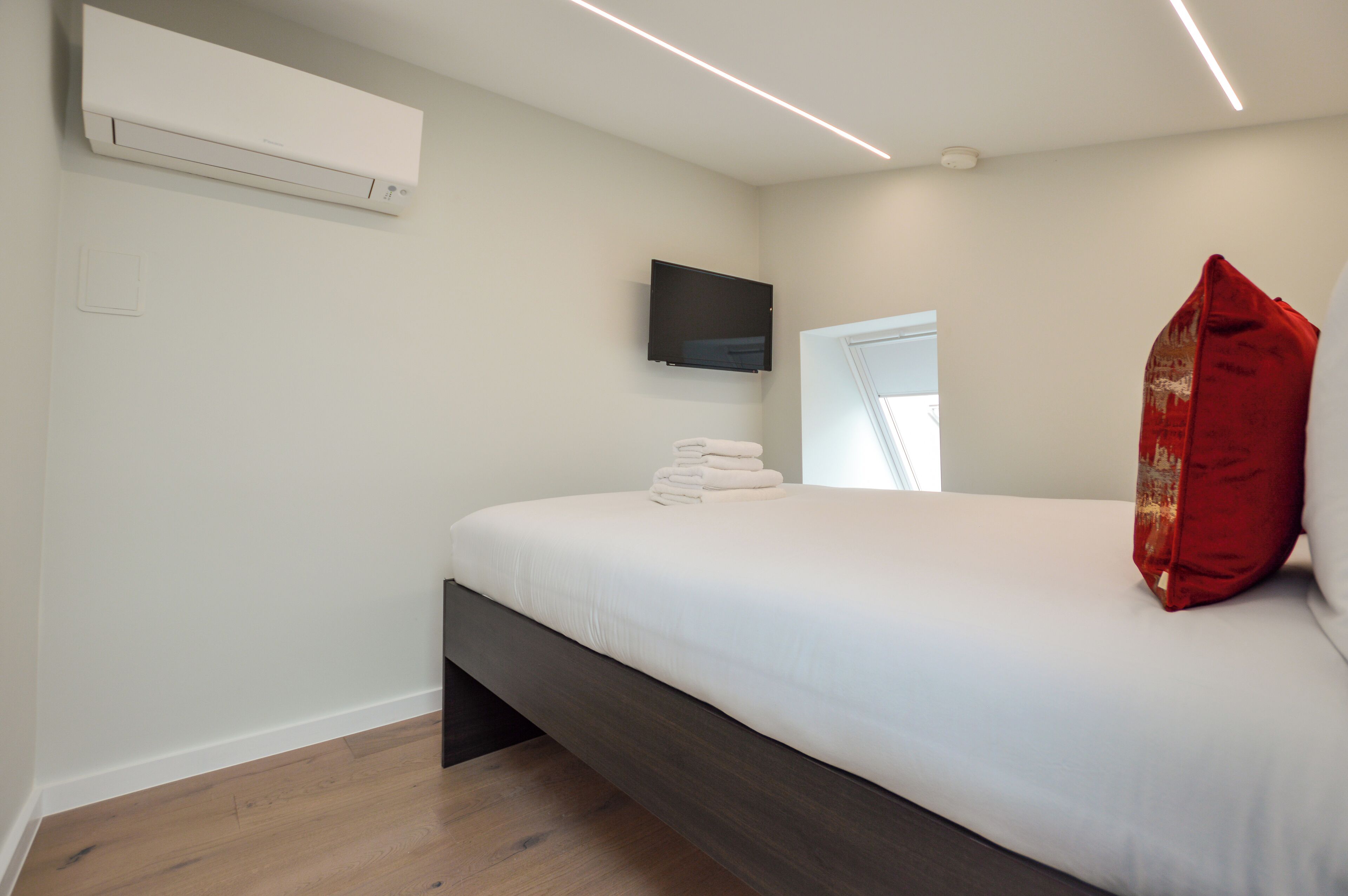 Moderni hotellihuone, jossa on sänky, seinälle asennettu taulutelevisio ja ikkuna, josta tulee luonnonvaloa.