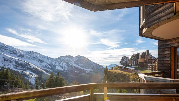 Un balcon en bois offrant une vue sur des montagnes enneigées et une ville.