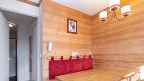 Une pièce aux murs lambrissés, avec une table et des chaises en bois, un banc rouge, un téléphone et un tableau encadré accroché au mur.