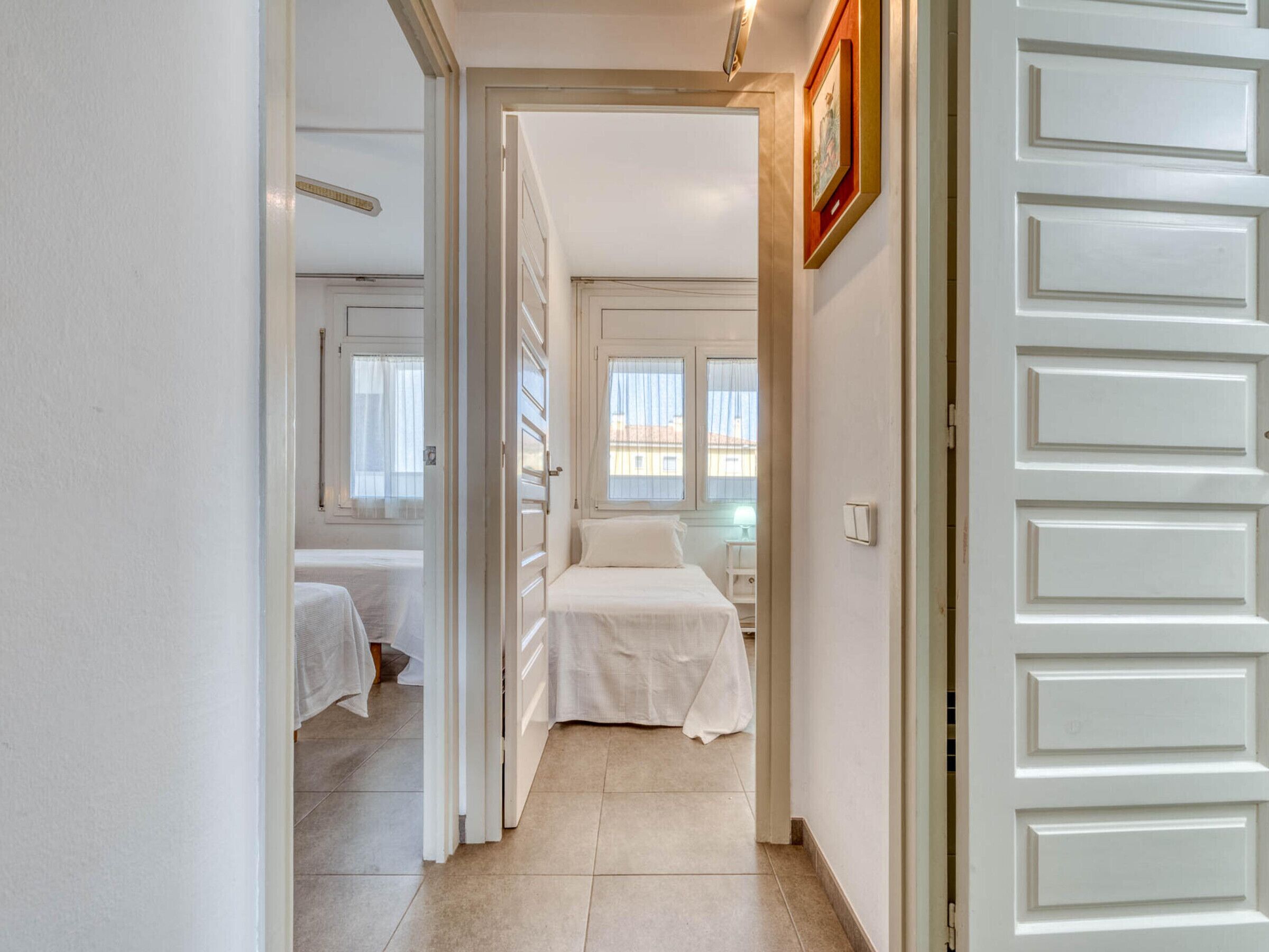 Un pasillo que conduce a un dormitorio con cama, mesita de noche y ventana.