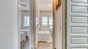 Un pasillo que conduce a un dormitorio con cama, mesita de noche y ventana.