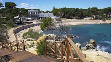 A wooden boardwalk leading to a beach with a clear view of the sea and a building in the background.
