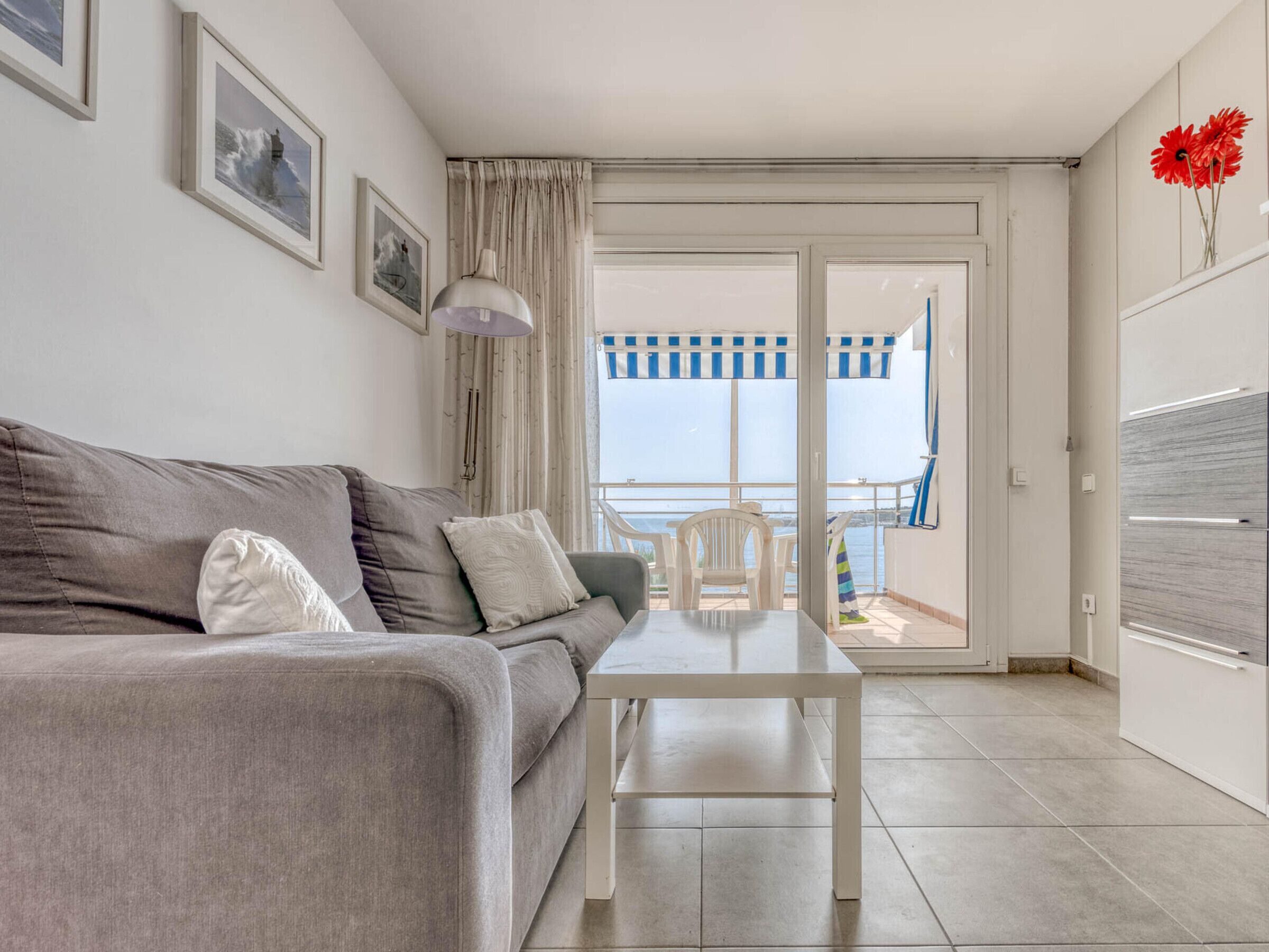 Ein modernes Wohnzimmer mit grauem Sofa, einem weißen Couchtisch und Meerblick durch eine Schiebetür.