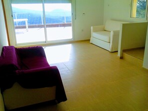 Ein Wohnzimmer mit einem weißen Sofa, einem violetten Sofa und einem weißen Sessel. Eine Glastür führt auf einen Balkon.