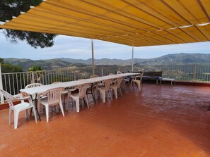 An outdoor terrace with a table and chairs, a yellow canopy, and a view of distant mountains.