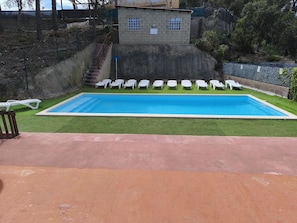 A rectangular swimming pool with a clear blue water surface, surrounded by a green lawn and white lounge chairs.