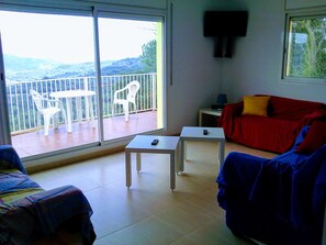 Une pièce avec un balcon, un canapé rouge, un canapé bleu, une petite table et une table blanche.