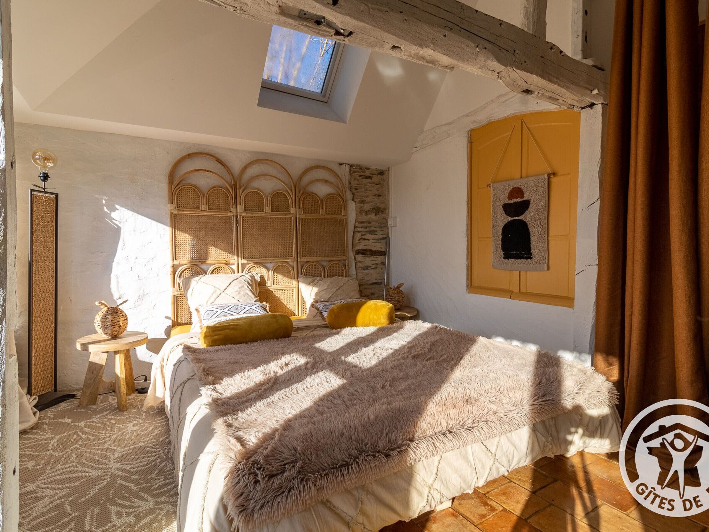 Ein gemütliches Schlafzimmer mit einem großen Bett, einem Oberlicht, einem rustikalen Kopfteil und einem kleinen Fenster.