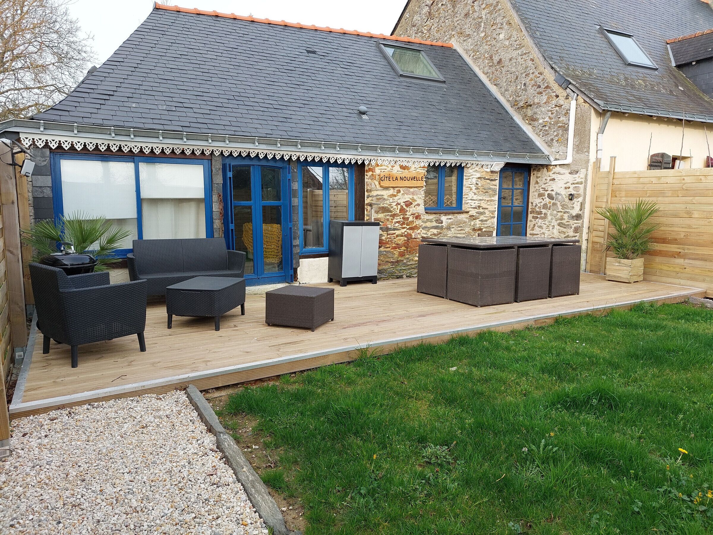 Ein Haus mit einer Terrasse, die Gartenmöbel, eine Steinmauer und ein blau gerahmtes Fenster zeigt.