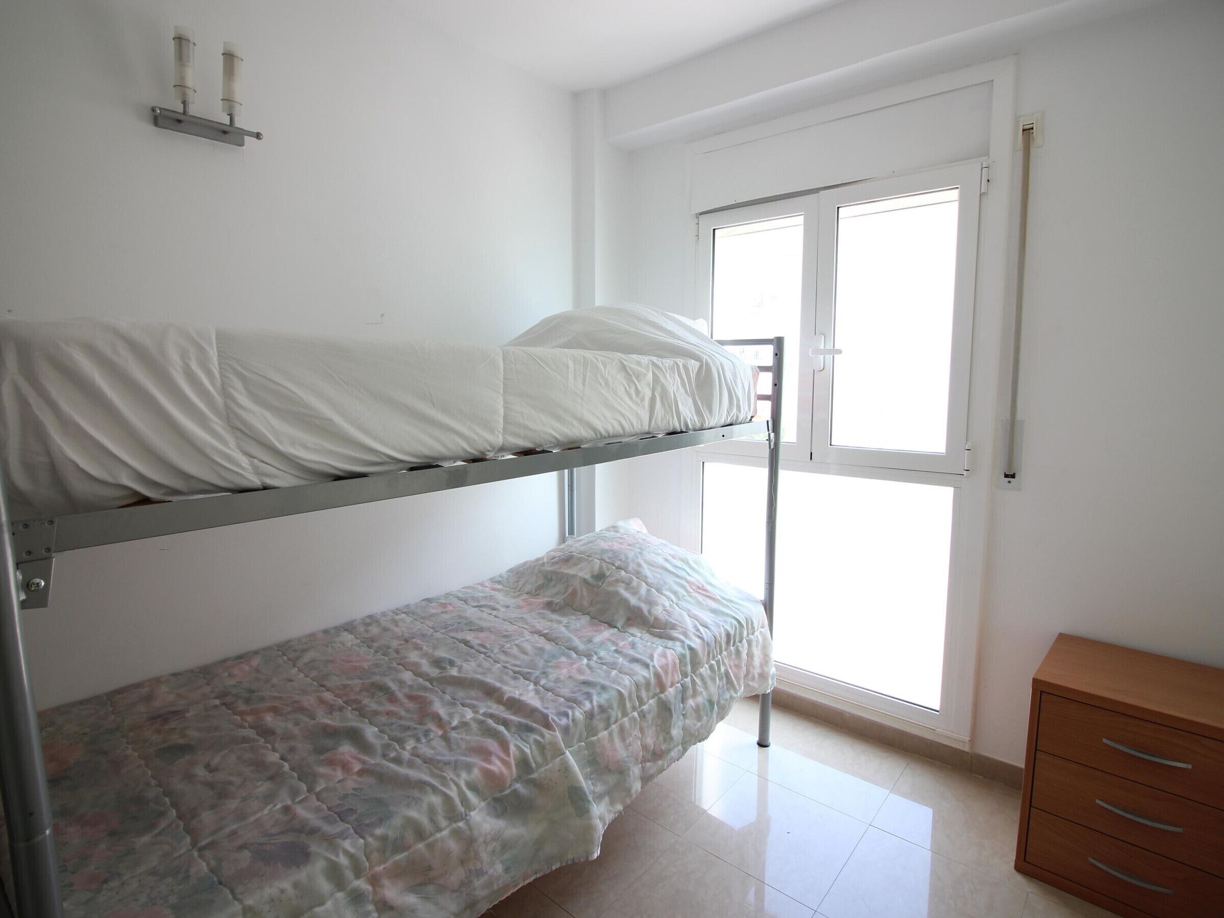 A bedroom with a bunk bed, a single bed, a wooden dresser, and a window with blinds.