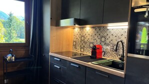A modern kitchen with a black countertop, a red coffee machine, and a window with a view of trees. - Renovated apartment with pool in Samoëns (Samoëns)