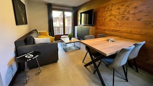 A modern living room with a sofa, a dining table, and chairs. There is a television on the wall and a window with curtains. - Renovated apartment with pool in Samoëns (Samoëns)