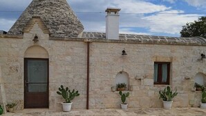 A stone building with a conical roof, potted cacti, and a tiled courtyard. - Trulli of the Chain (Martina Franca)
