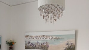 A bedroom with a bed, pillows, a nightstand, a lamp, a wall-mounted painting, and a chandelier.