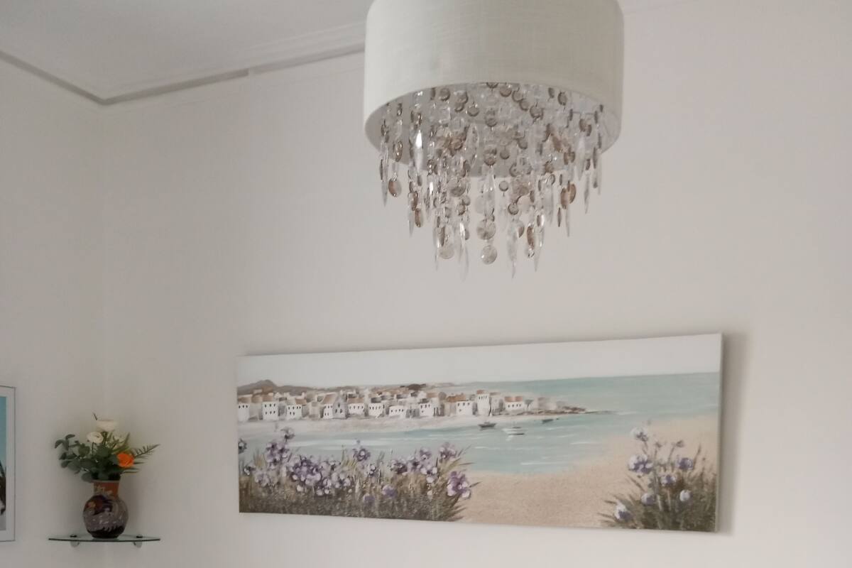 Et soveværelse med seng, puder, et natbord, en lampe, et ophængt maleri og en lysekrone.