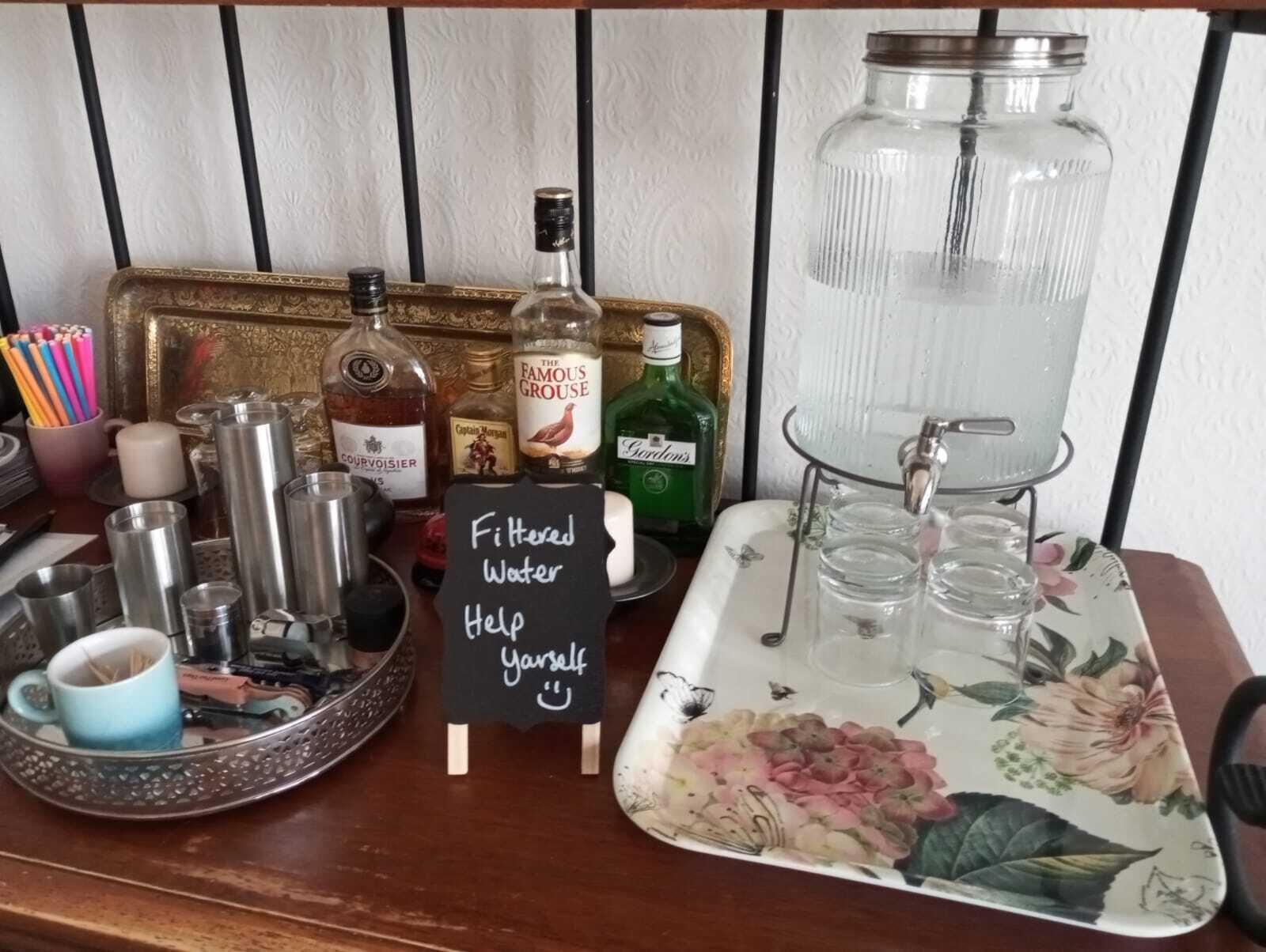 Un bar équipé de différentes bouteilles, d’un distributeur d’eau et d’un plateau avec des verres.
