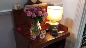 A wooden side table with a lamp, a vase of flowers, a clock, and a sign that says "Strangers, Leave as friends."