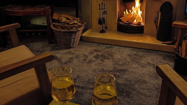 A cozy living room with a fireplace, a piano, and two glasses of wine on a table.