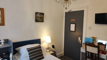 Een hotelkamer met een bed, een bureau, een stoel, een kroonluchter, een televisie en een deur.