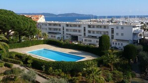 A hotel with a swimming pool, surrounded by greenery and overlooking a marina with boats.