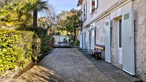 Un patio con un sendero de grava, bancos y un edificio con puertas y ventanas.