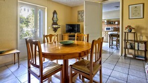 Un comedor con mesa y sillas de madera, un televisor y una cocina al fondo.