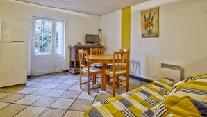 Ein gemütlicher Raum mit Esstisch, Stühlen, Fernseher und einem Bett mit gestreifter Bettwäsche.