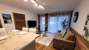 Ein modernes Wohnzimmer mit Holzboden, einer Couch, einem Fernseher und einem Essbereich mit Tisch und Stühlen.