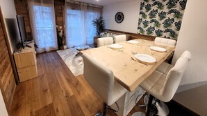 Ein Essbereich mit einem Holztisch, gedeckt für vier Personen, weißen Stühlen, einer Uhr an der Wand und einer Pflanze in der Ecke.