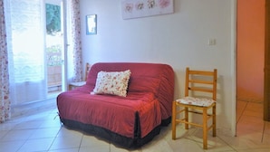Un dormitorio con una cama roja, una silla de madera, una ventana con cortinas y un cuadro colgado en la pared.