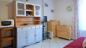 Una habitación con kitchenette, una cama, un televisor y un reloj en la pared.