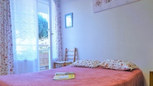 Un dormitorio con cama, una silla, una ventana con cortinas y un cuadro colgado en la pared.