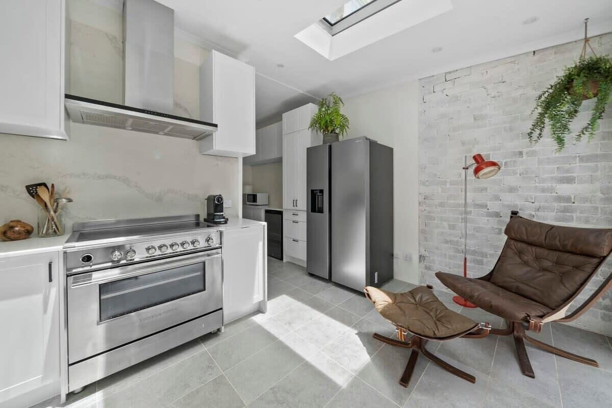 A modern kitchen with stainless steel appliances, a hanging plant, and a unique brown leather chair.