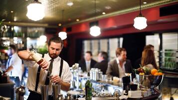 A bar area with a bartender preparing drinks, a bar counter with various bottles and glasses, and a bowl of fruit.